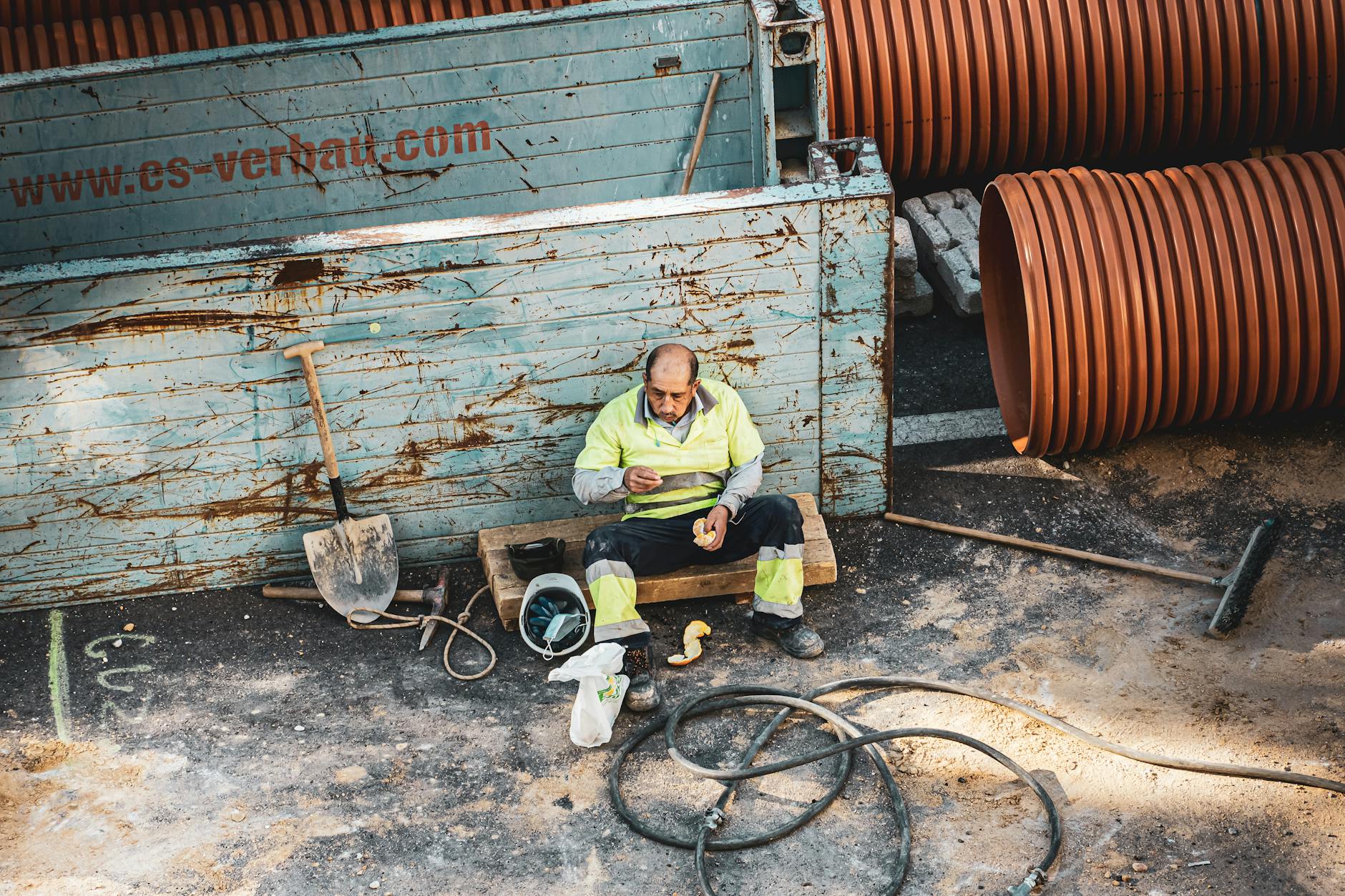 A construction worker sitting on a site in Madrid, enjoying a break amid tools and pipes.