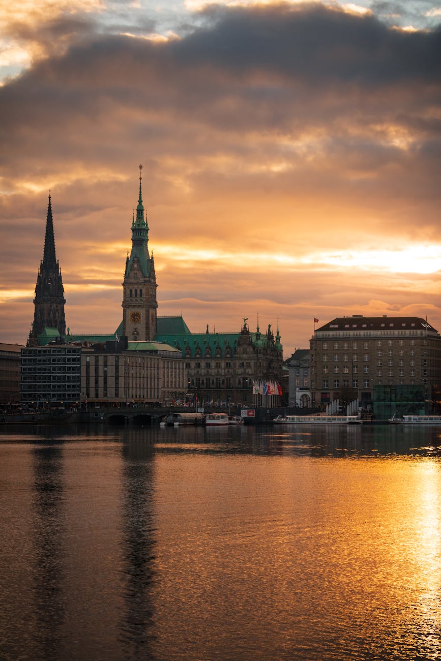 Dramatic view of Hamburg's skyline at sunset featuring iconic architecture and vivid water reflections.