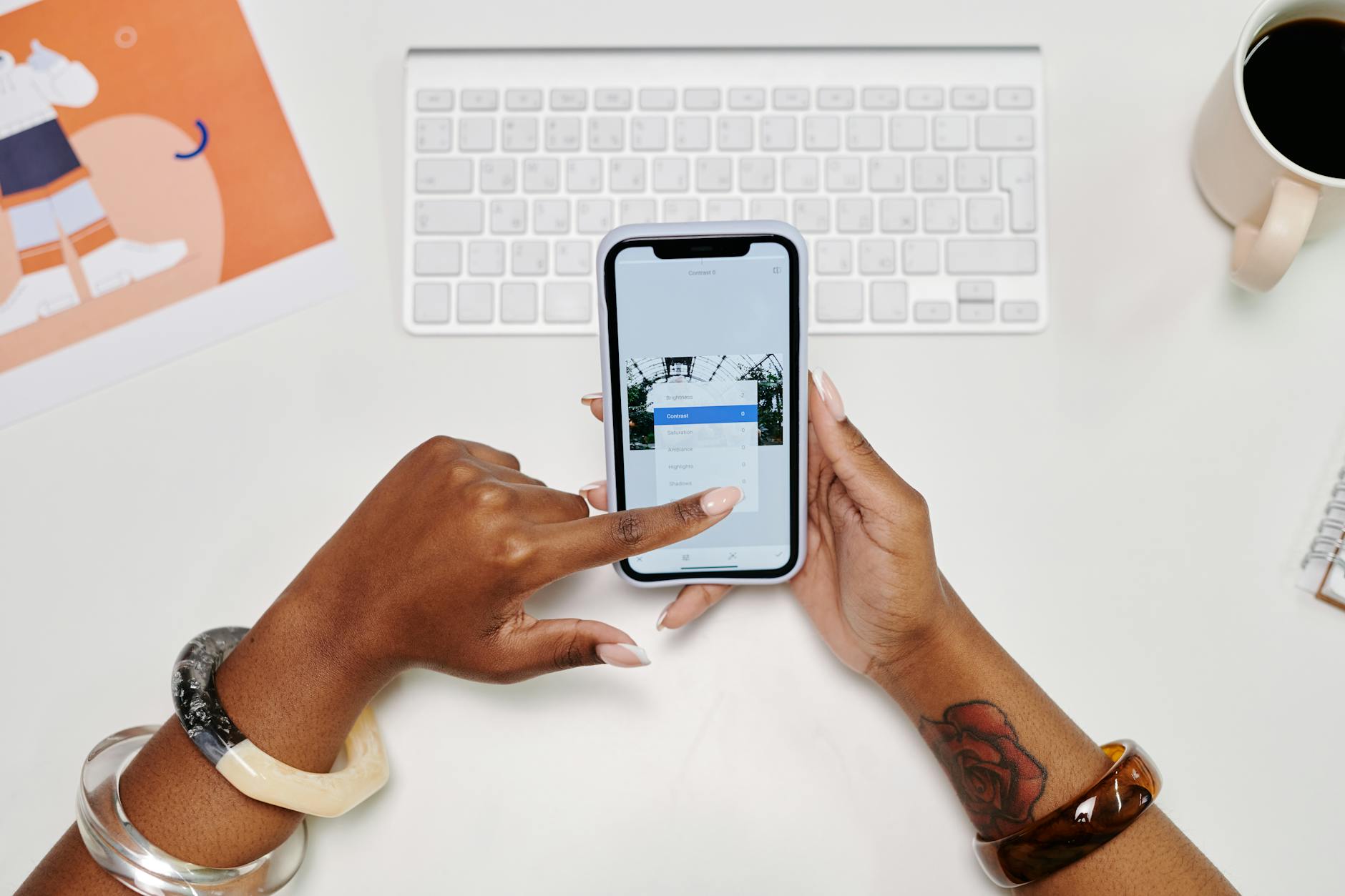 Close-up of hands using a smartphone at a desk with a keyboard and coffee cup.