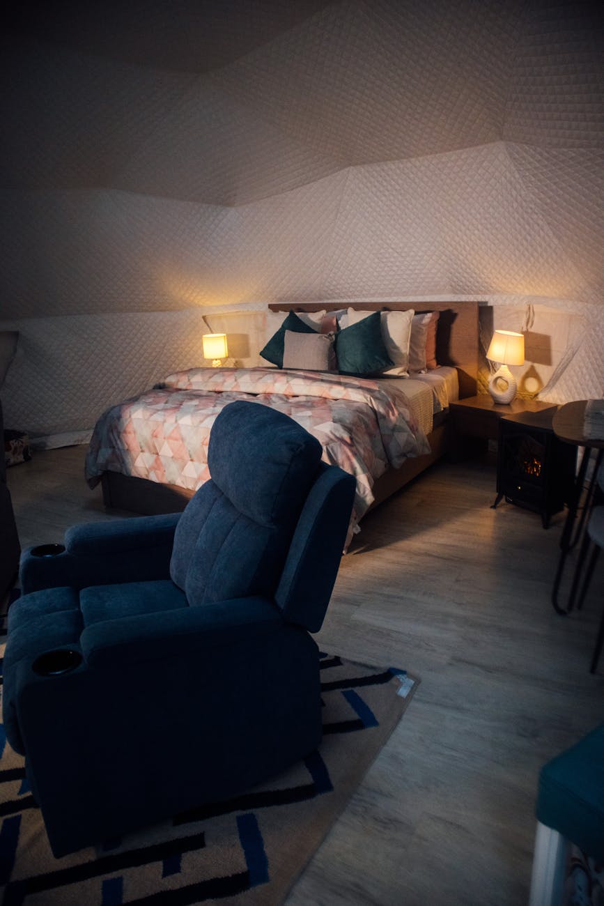 Stylish bedroom with cozy bed, blue recliner, and ambient lighting. Perfect for relaxation.