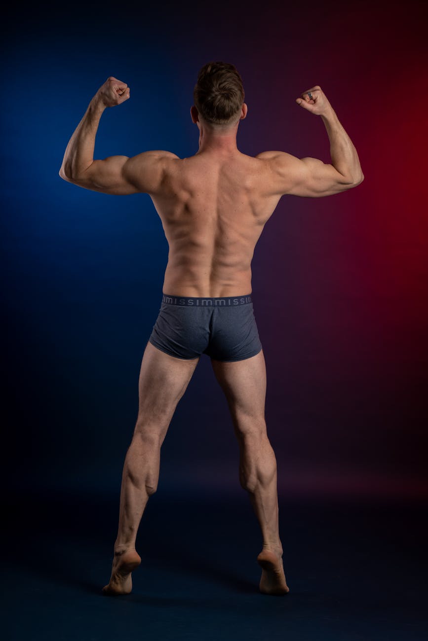 Strong muscular man flexing his back muscles in moody lighting, showcasing physical fitness.