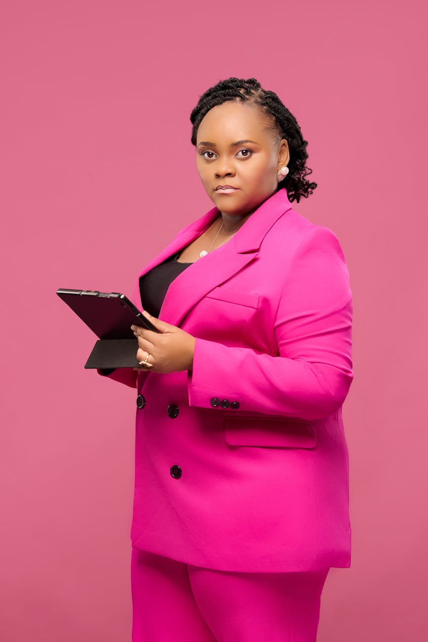 Portrait of a confident businesswoman in vibrant pink holding a tablet, set against a matching pink background.