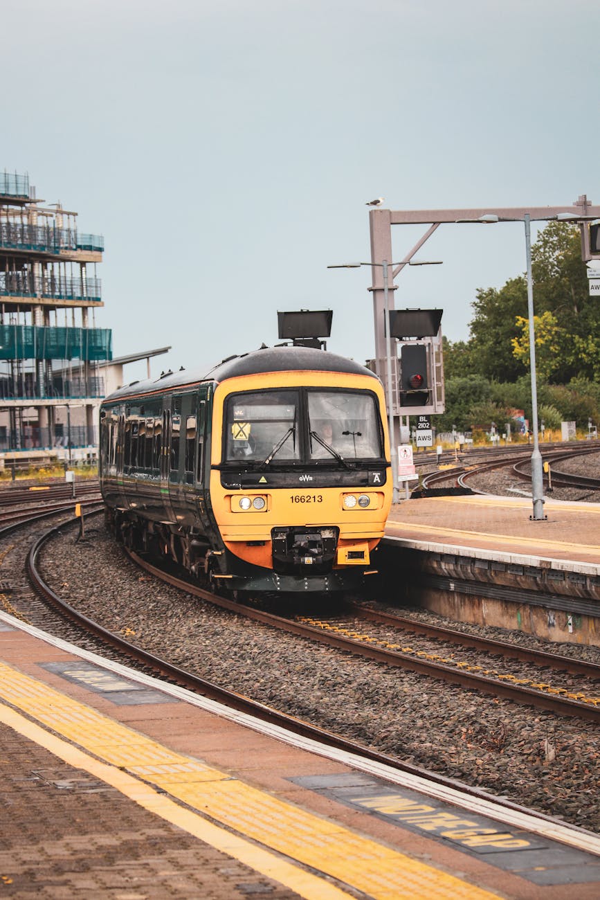 A modern train arriving at a city railway station on a sunny day, featuring tracks and urban architecture.