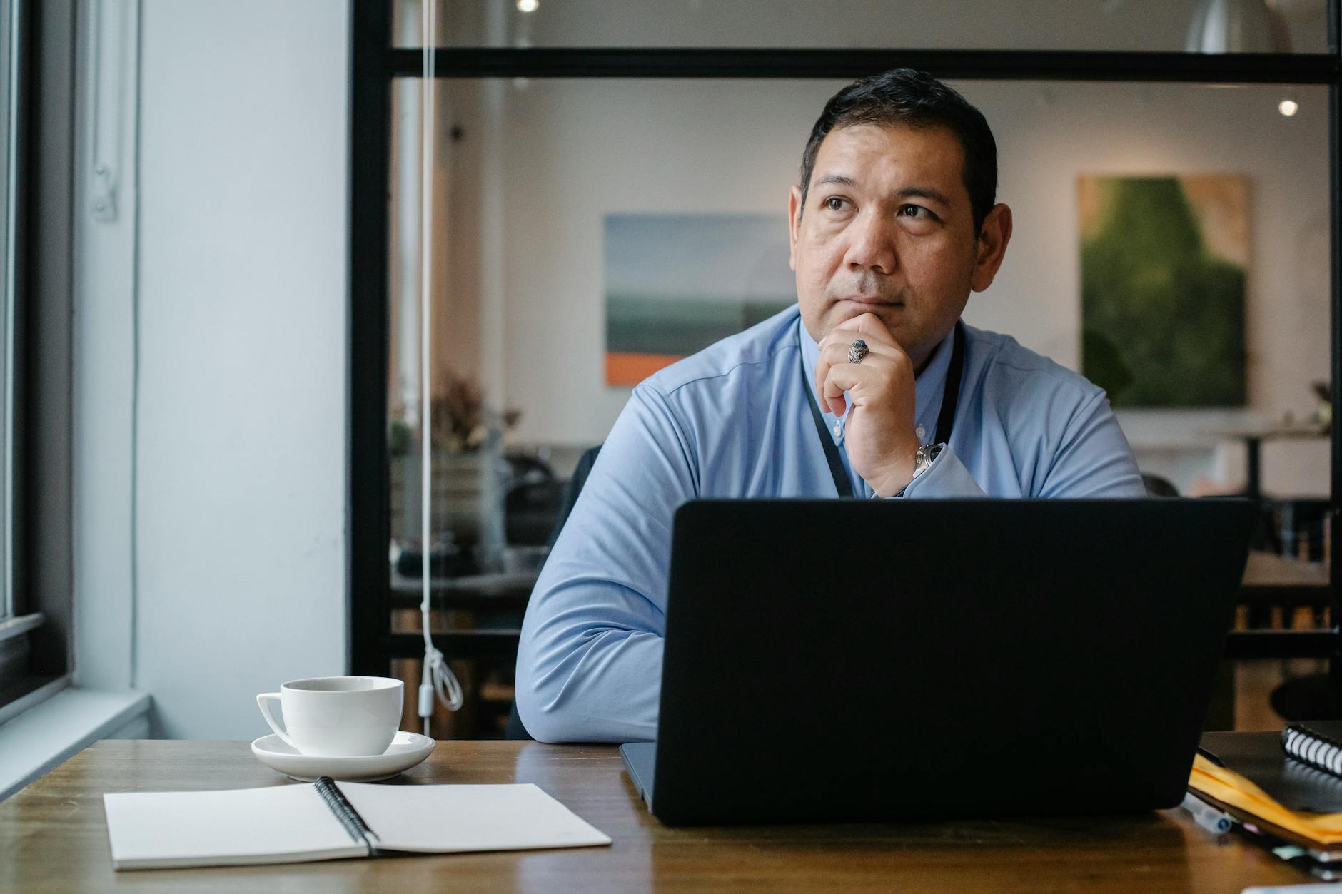 A businessman deep in thought while working on a laptop in a modern office setting.