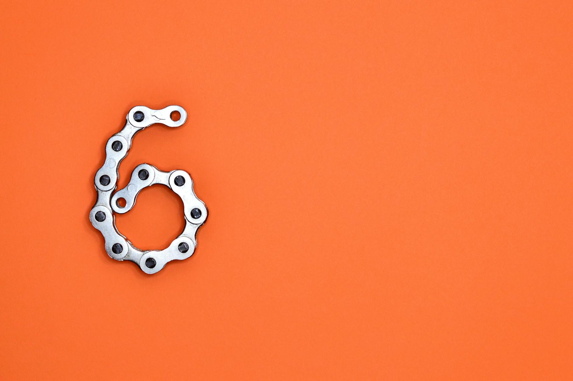 A creative display of a bike chain forming the number six against a vibrant orange backdrop.