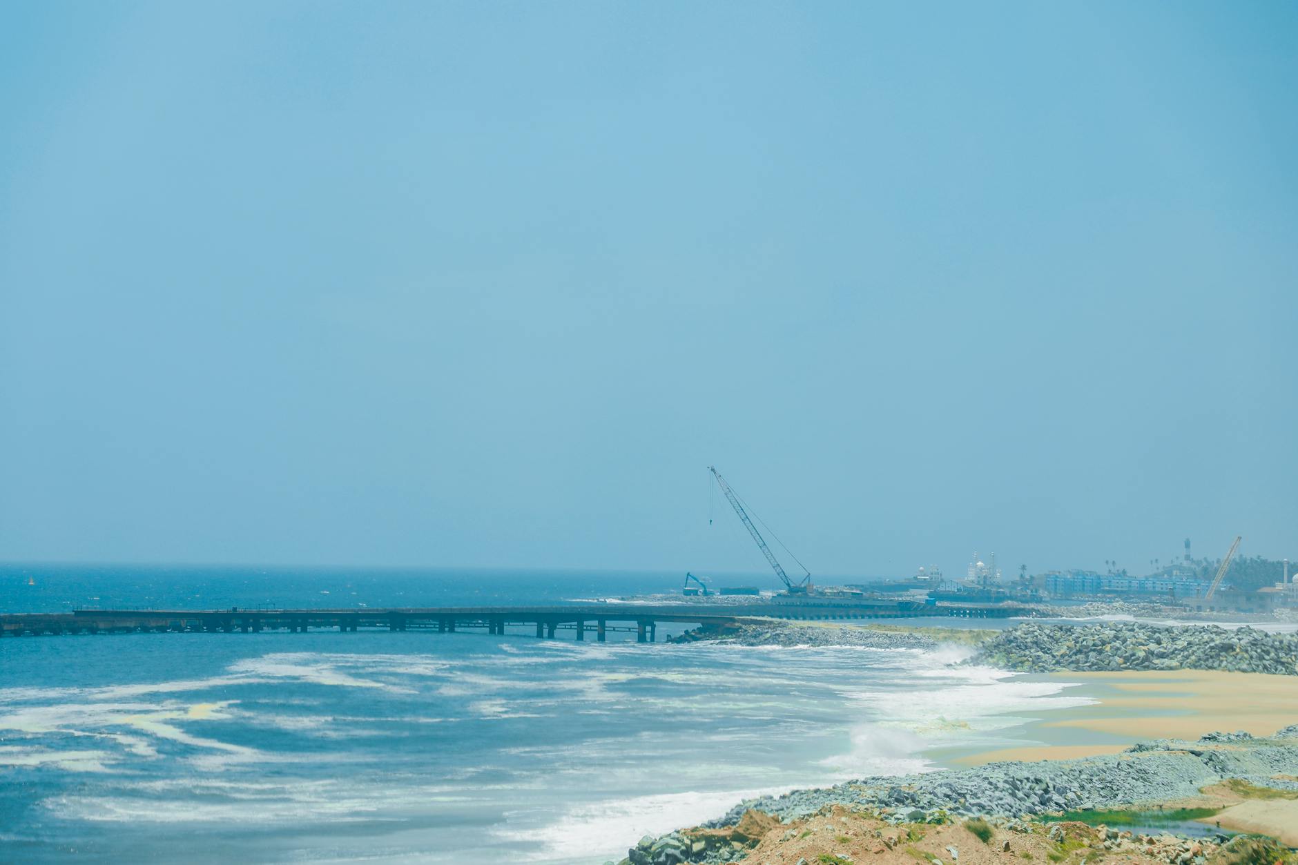 Ocean waves crashing on Thiruvananthapuram beach with construction in the distance.