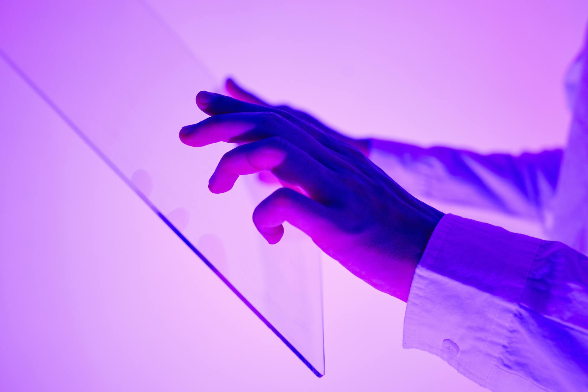 Close-up of hands interacting with a transparent glass interface in purple light.