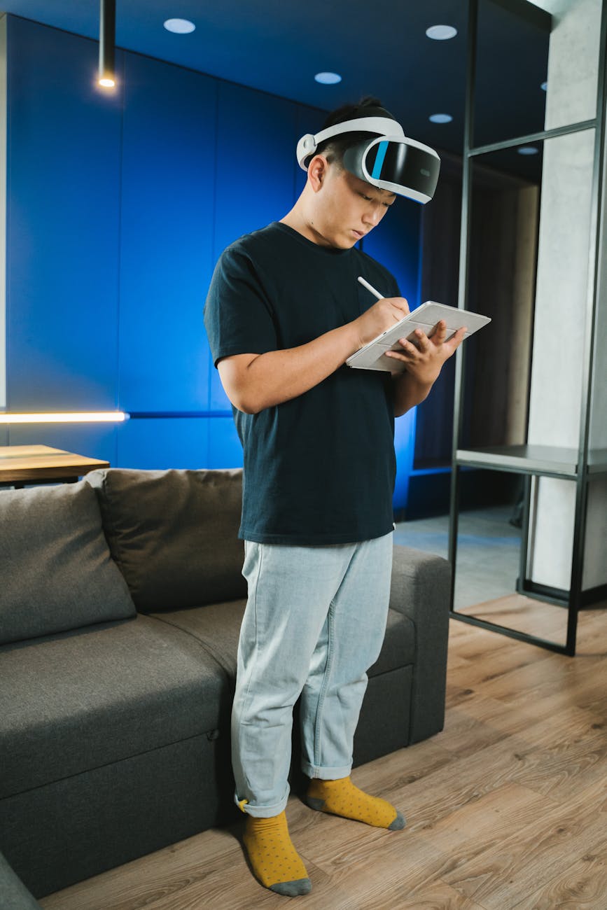 Adult man using augmented reality headset while writing on a digital tablet indoors.
