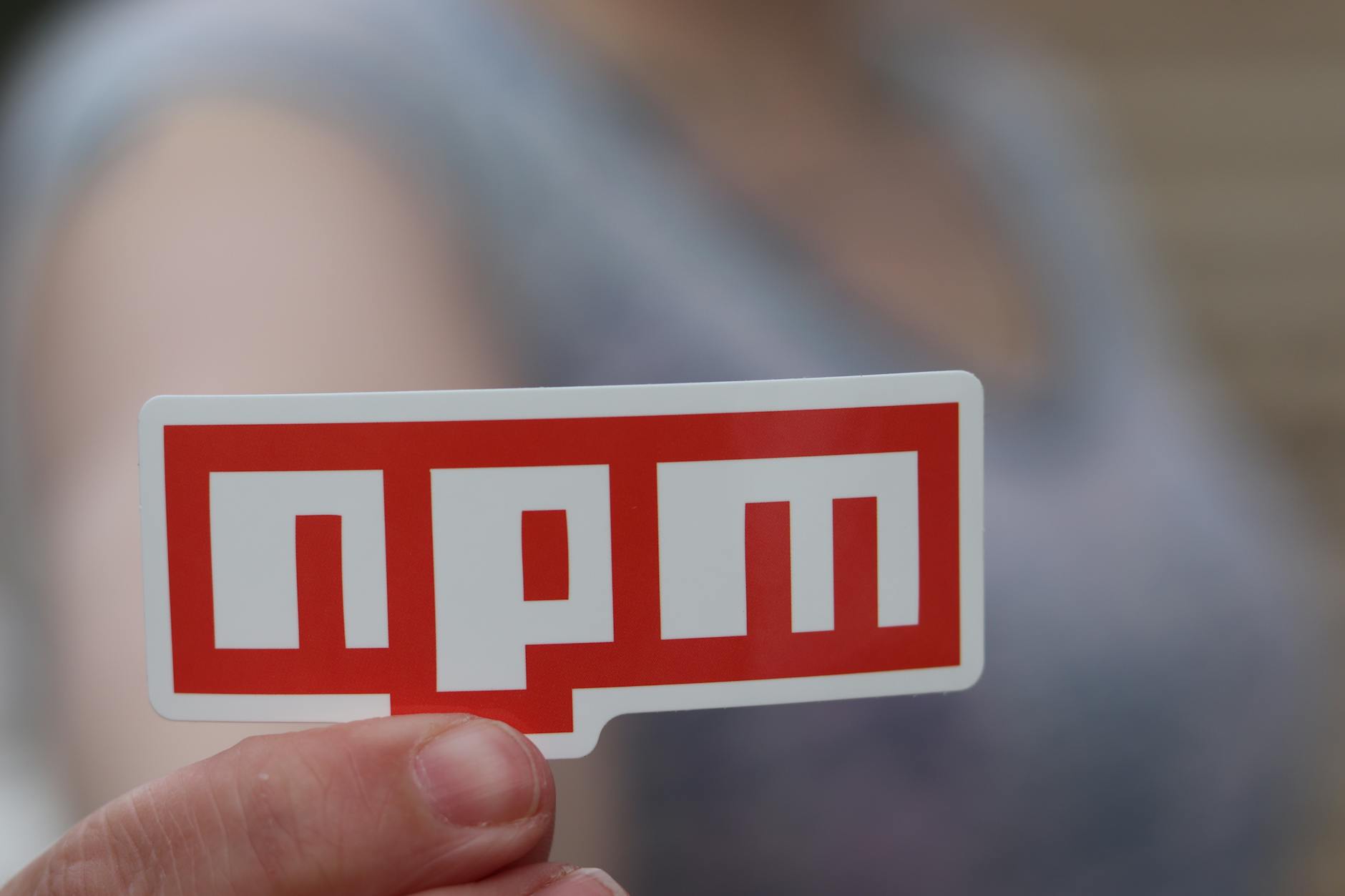 Blurred background close-up of a hand holding an npm sticker, ideal for web development themes.