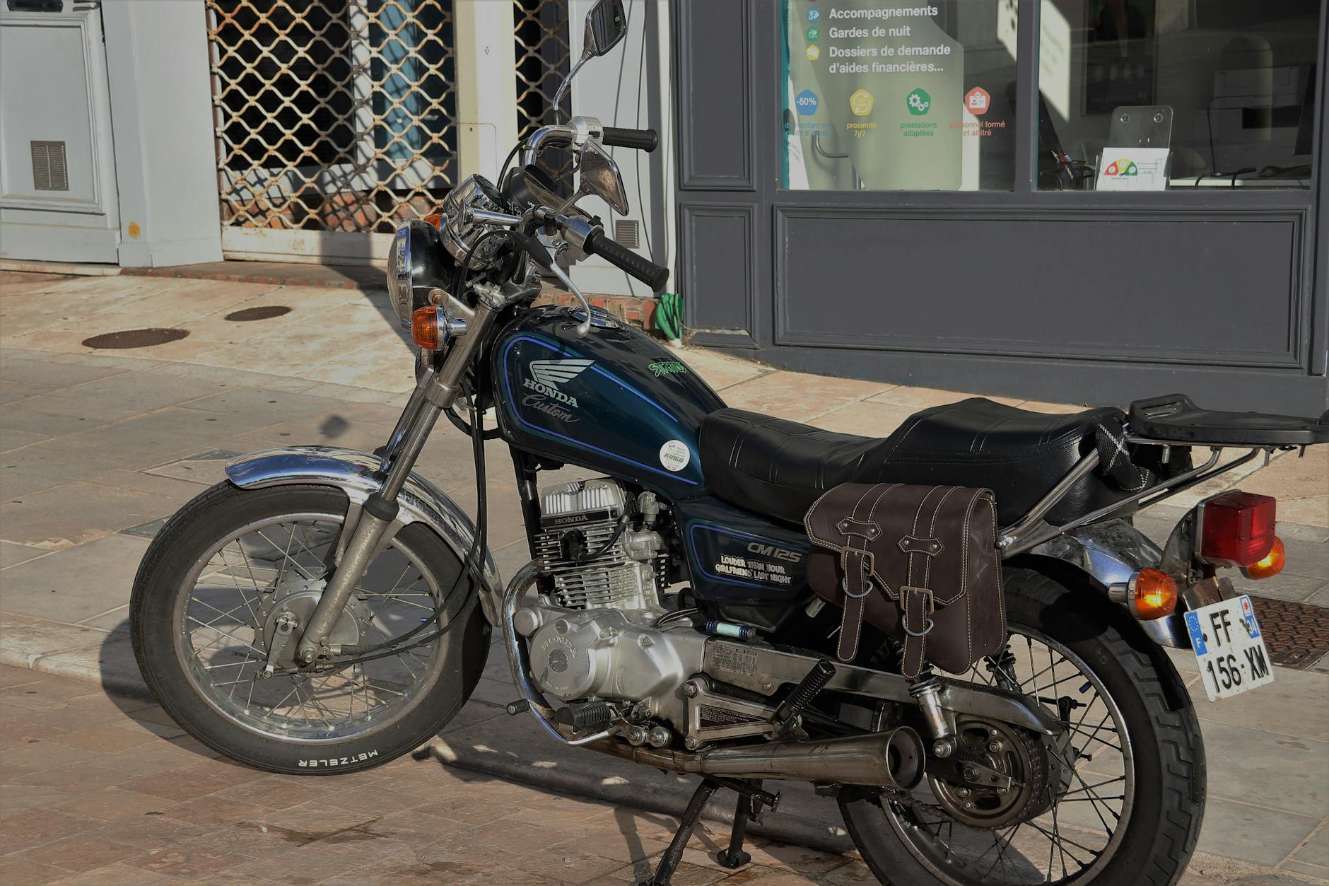 Vintage Honda CM 125 motorcycle parked on a sunny street with a side saddlebag.