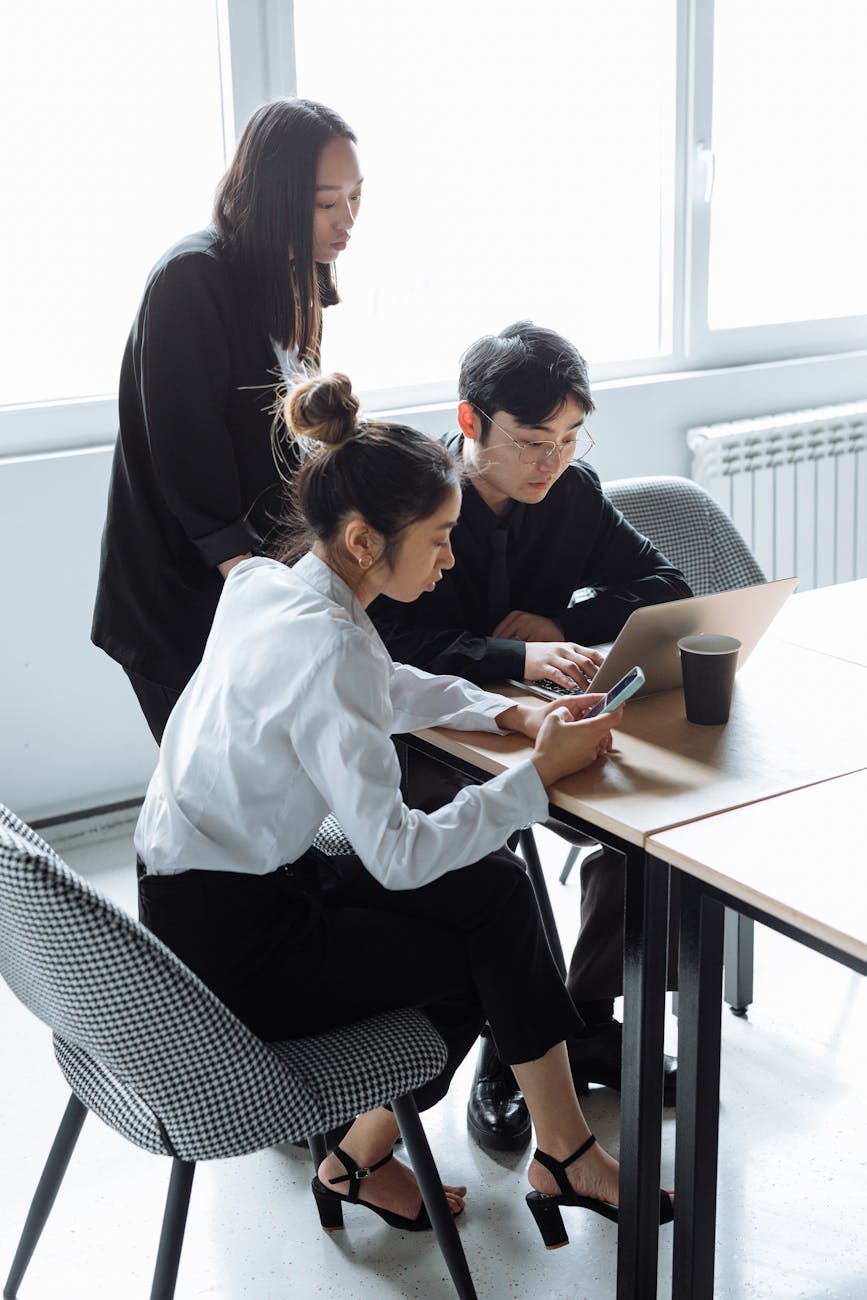 Three colleagues collaborating in a modern office setting with laptops and phones.