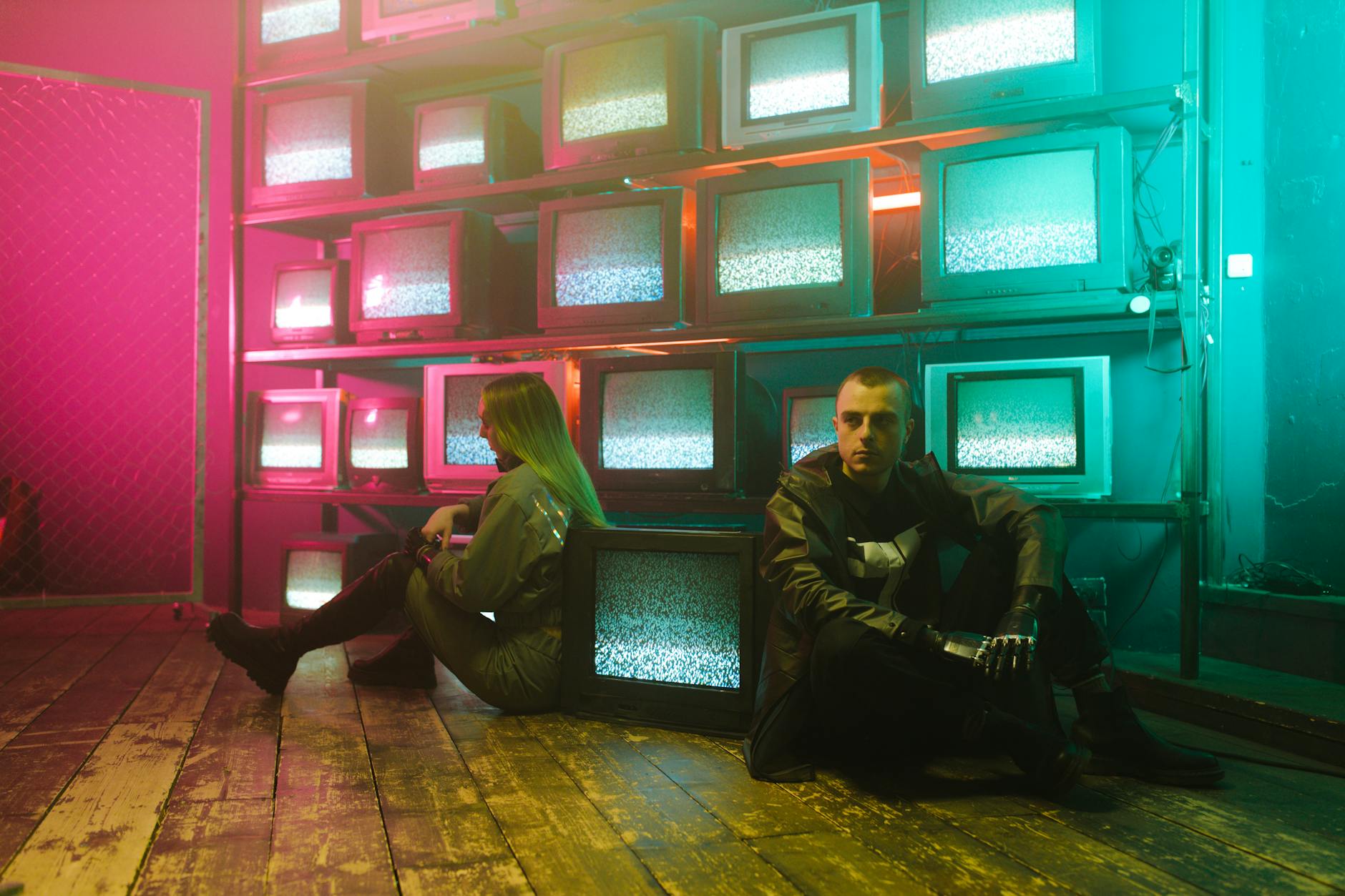 Two individuals in a cyberpunk setting with neon lighting and stacked television screens.