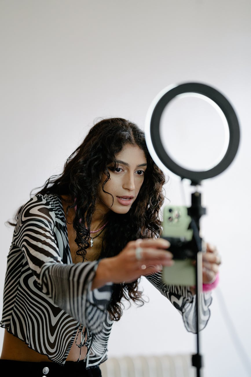 Woman adjusts smartphone on tripod with ring light indoors, perfect lighting for video content.