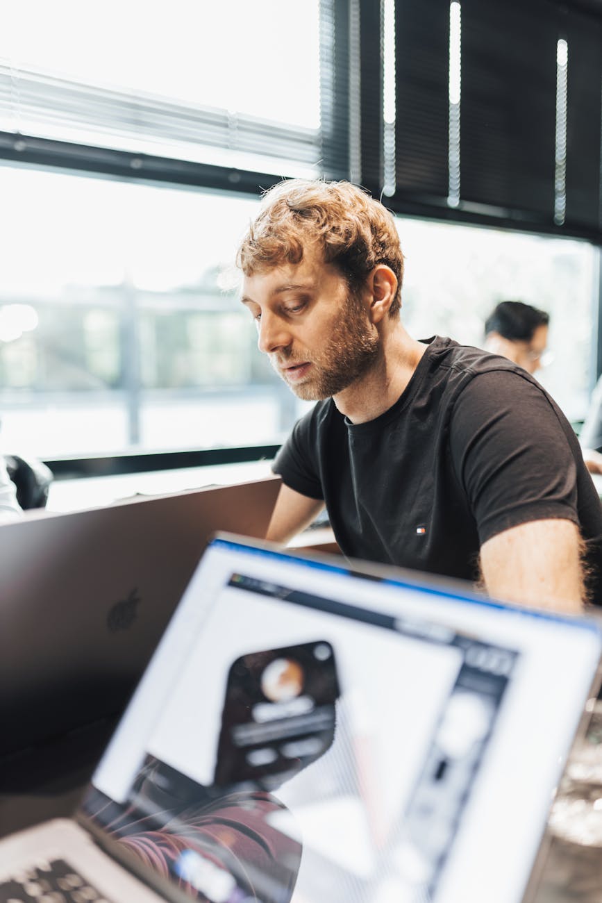 Focused man working with a laptop in a modern office setting, showcasing technology and productivity.