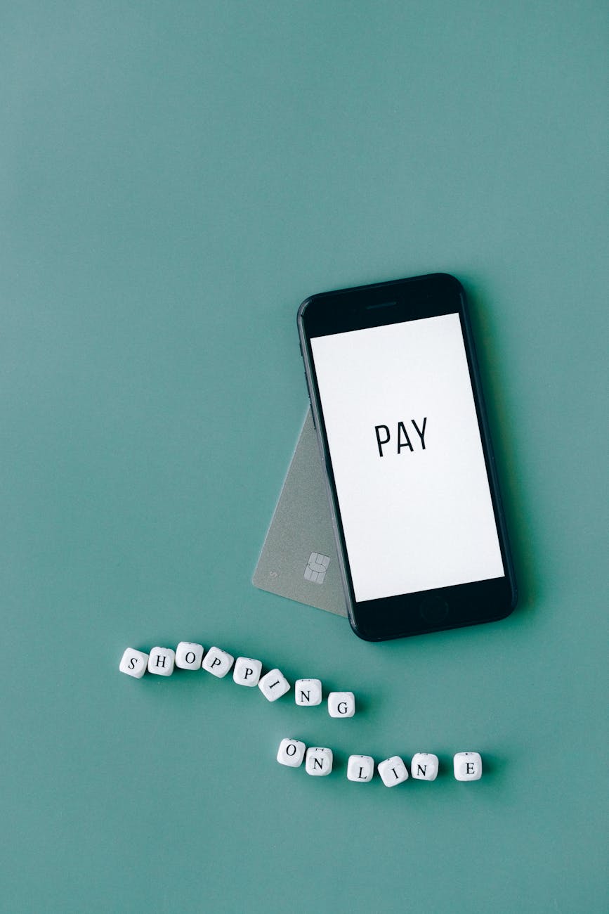 Minimalist flat lay of a smartphone with 'PAY' screen and payment card on a green background, emphasizing online shopping.